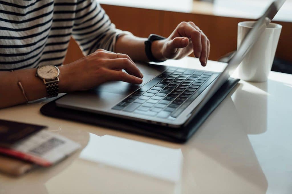 A persons hands typing on a laptop.