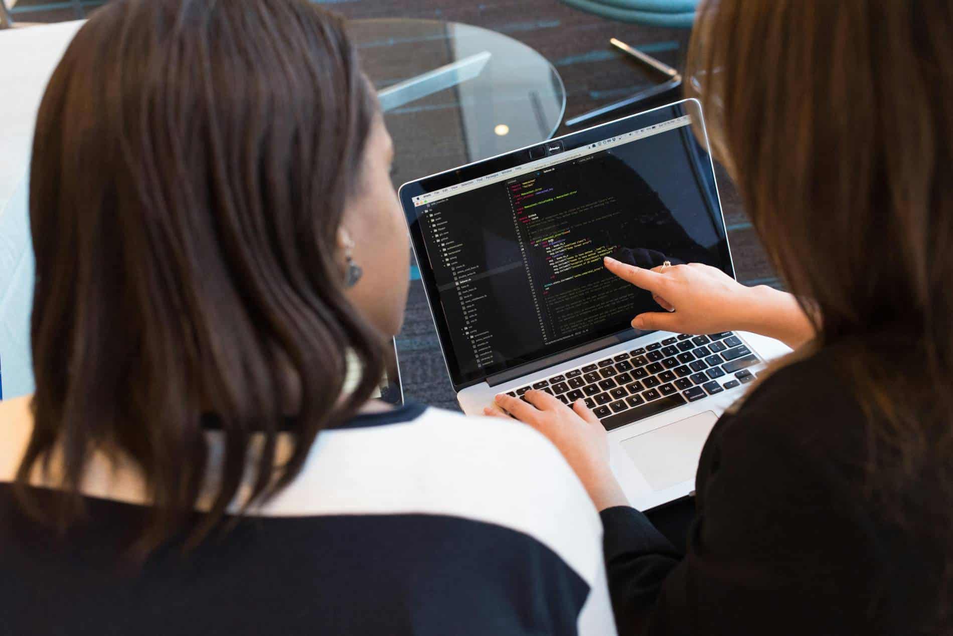 Two people looking at a laptop with one person pointing to some data on the screen.