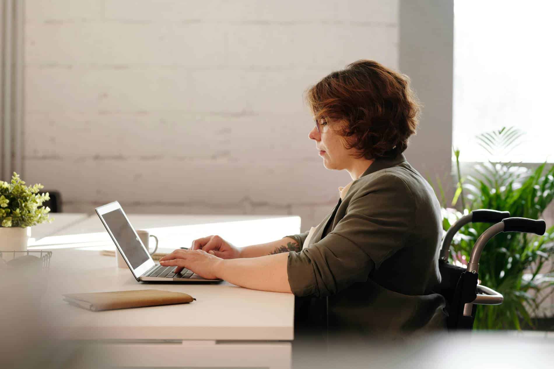 A woman in a wheelchair typing on a laptop.