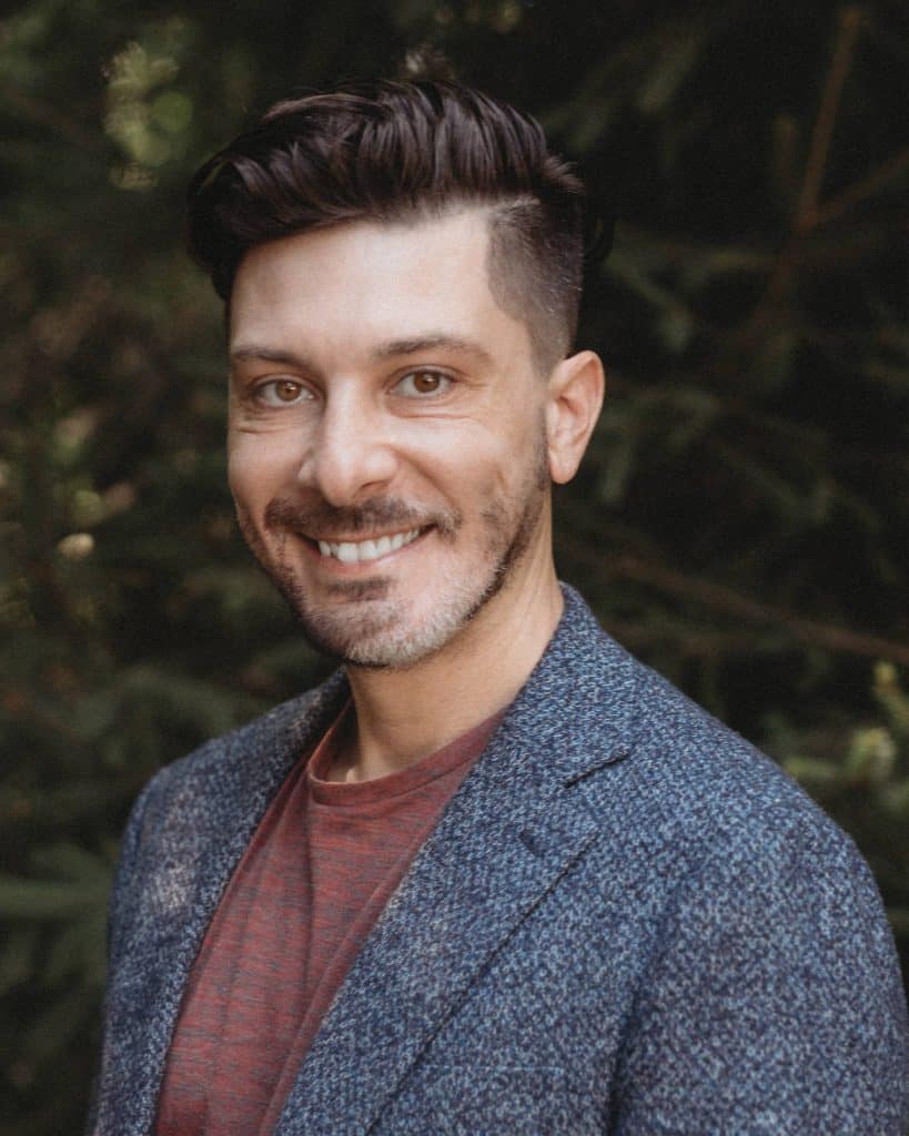 An outdoor headshot of Anthony wearing a red shirt and grey suit jacket.