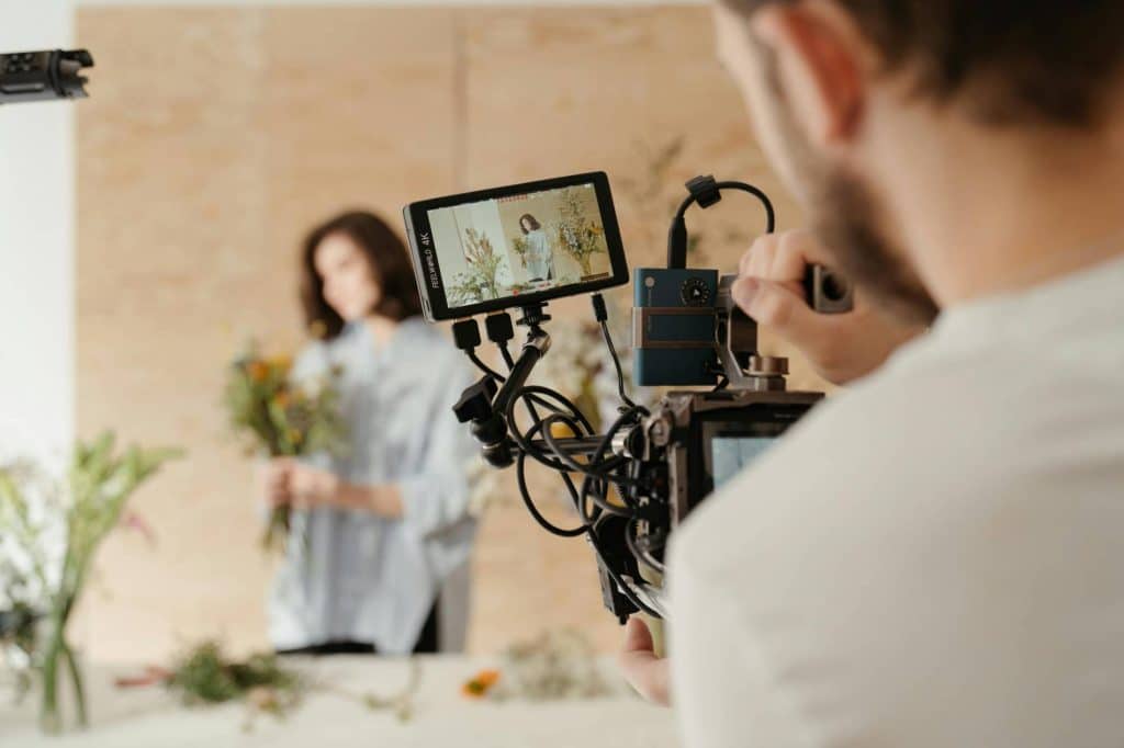 An-over-the-shoulder look at a cameraman creating a marketing video for a small business owner.