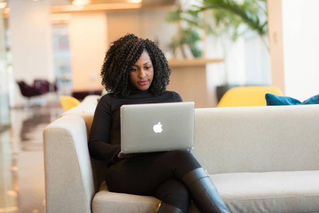 A woman with a laptop sitting on a white sofa. She is emailing to request backlink reinstatement.